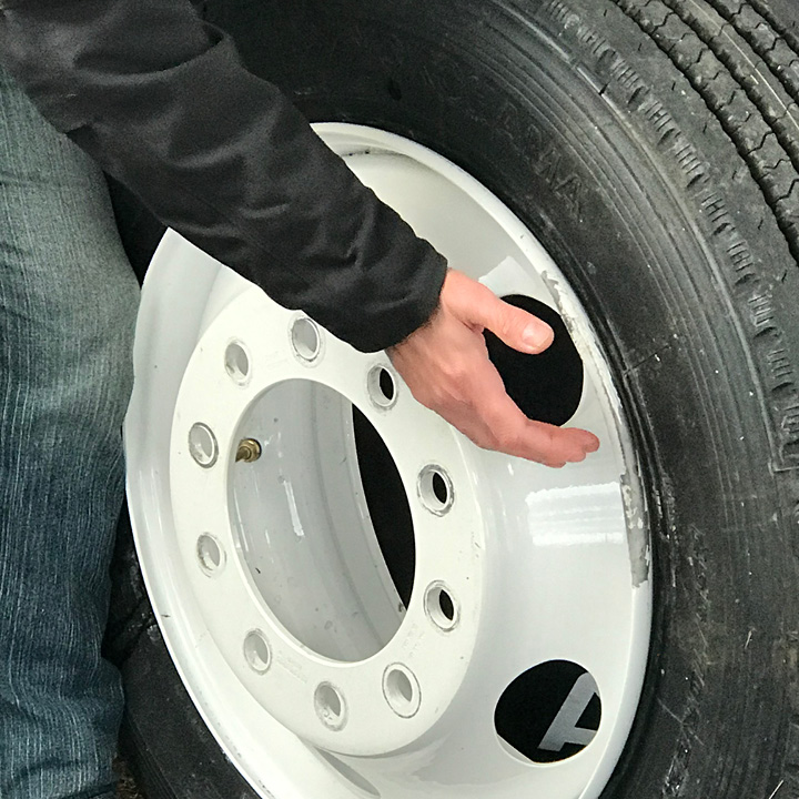 Hand pointing to a white painted steel truck wheel rim